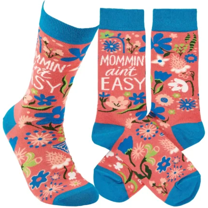 A pair of colorful woven socks from our Mother's Day Collection displaying unique hand illustrated designs of flowers with a fun mom-themed sentiment that reads "Mommin' Ain't Easy." Socks feature a one size fits most design made with cotton, nylon, and spandex. Our Mommin' Ain't Easy socks come with a header card and a clear plastic hanger for display. A fun Mother's Day gift and accessory perfect for everyday self-expression.