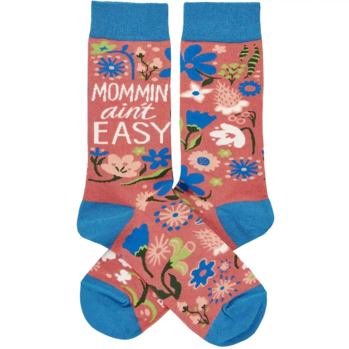 A pair of colorful woven socks from our Mother's Day Collection displaying unique hand illustrated designs of flowers with a fun mom-themed sentiment that reads "Mommin' Ain't Easy." Socks feature a one size fits most design made with cotton, nylon, and spandex. Our Mommin' Ain't Easy socks come with a header card and a clear plastic hanger for display. A fun Mother's Day gift and accessory perfect for everyday self-expression.